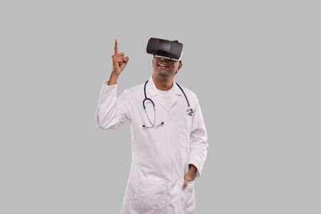 Doctor Wearing VR Glasses Pointing Up Isolated. Indian Man Doctor Virtual Reality Good Ideaの写真素材