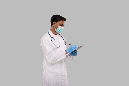 Doctor Writing in Clipboard Wearing Medical Mask and Gloves. Indian Man Doctor Clipboard Isolatedの写真素材