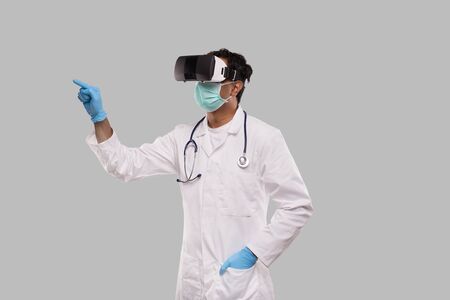 Doctor Wearing VR Glasses, Medical Mask and Gloves Tapping Isolated. Indian Man Doctor Pointing in Virtual Realityの写真素材