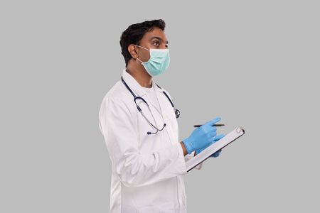 Doctor Writing Down Good Idea in Clipboard Wearing Medical Mask and Gloves. Indian Man Doctor Clipboard Isolatedの写真素材