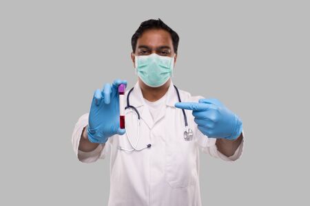 Indian Man Doctor Pointing at Blood Tube Analysis Wearing Medical Mask And Gloves. Science, Medical Concept. Isolated.の写真素材