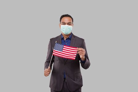 Businessman Holding American Flag Wearing Medical Mask. Indian Businessman Standing Full Length with USA Flag in Handsの写真素材