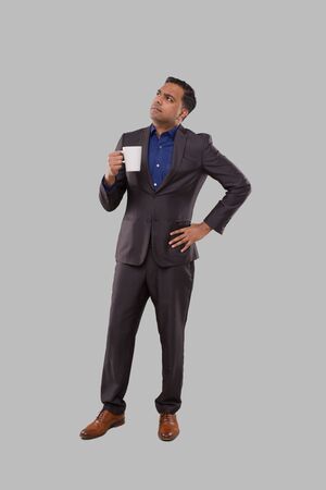 Businessman Watching Up Holding Coffee Cup. Indian Businessman Standing Full Length in Suit with Coffee Cupの写真素材