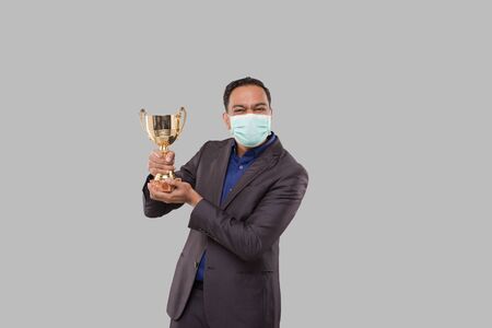 Businessman Holding Trophy Wearing Medical Mask. Indian Business man Standing with Trophy in Handsの写真素材