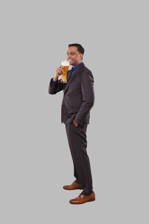 Businessman Drinking Beer from Glass. Indian Business man Standing Full Length with Beer in Handの写真素材
