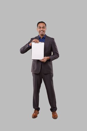 Businessman Holding Clipboard Watching in Camera Isolated. Indian Business man Standing Full Length with Clipboard in Handsの写真素材