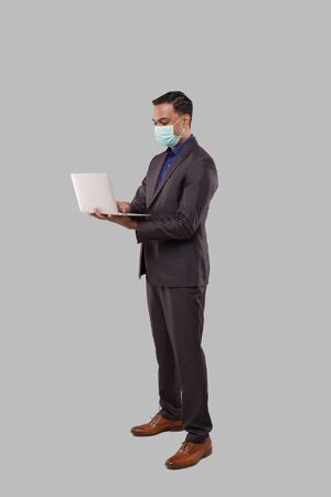 Businessman Using Laptop Green Screen Isolated Wearing Medical Mask. Indian Business man with Laptop in Hands. Online Business Conceptの写真素材