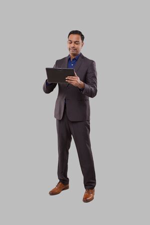 Businessman Using Tablet Isolated. Indian Business man Standing Full Length with Tablet in Handsの写真素材