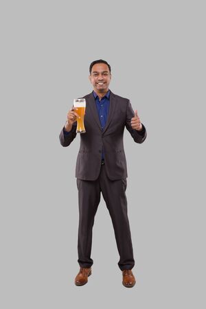 Businessman Holding Beer Glass Showing Thumb Up. Indian Business man Standing Full Length with Beer in Handの写真素材