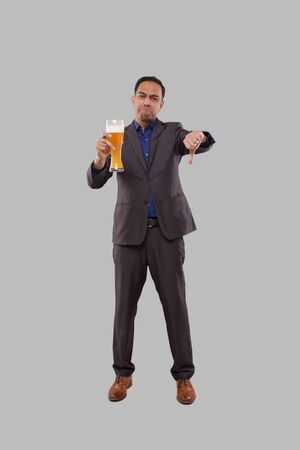 Businessman Holding Beer Glass Showing Thumb Down. Indian Business man Standing Full Length with Beer in Handの写真素材