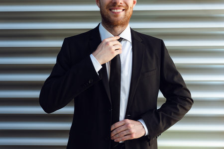 Businessman Straightens his Tie. Businessman Smilling in Black Suit.