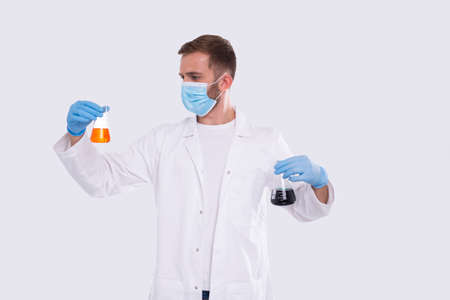 Male Doctor Examing Flask with Colorfull Liquid Wearing Medical Mask, Gloves Isolated. Science, Medical, Virus Concept. Man Doctor Smilling. Liquidの写真素材