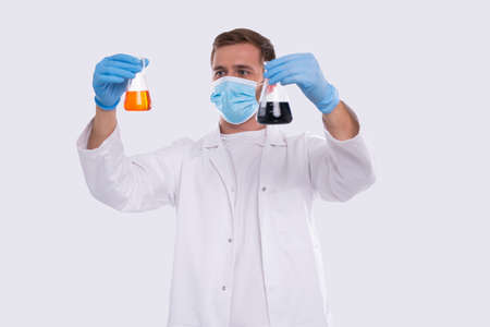 Male Doctor Examing Flask with Colorfull Liquid Wearing Medical Mask, Gloves Isolated. Science, Medical, Virus Concept. Man Doctor Smilling. Liquidの写真素材