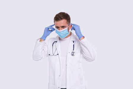 Male Doctor Puts on Medical Mask Wearing Gloves. Doctor Medical Workwear. Medical Concept. Doctor Holding Medical Maskの写真素材