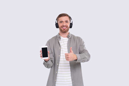 Man Listening to Music from Phone Showing Device and Thumb Up. Man Holding Phone. Isolatedの写真素材