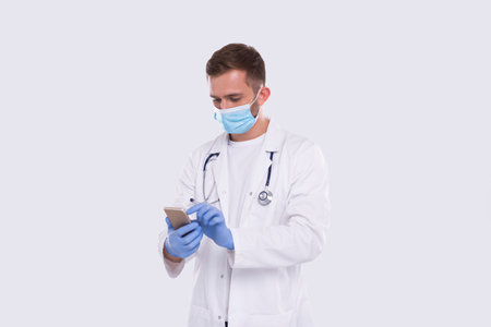 Doctor Standing Using Phone Wearing Medical Mask and Gloves Isolated. Man Texting on Phone. Technologyの写真素材