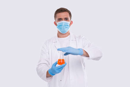 Male Doctor Showing Flask with Colorfull Liquid Wearing Medical Mask, Gloves Isolated. Science, Medical, Virus Concept. Man Doctor Smilling. Liquidの写真素材