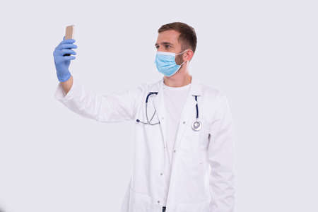Doctor Having Video Call on Phone Isolated Wearing Medical Mask and Gloves. Man Video Call. Man Using Phone.の写真素材