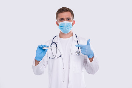 Doctor Showing Thermometer Wearing Medical Mask and Gloves Isolated. Man Doctor with Thermometer in Hands Pointing at It. Healthy Life, Doctor, Virus Conceptの写真素材
