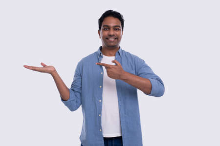Man Holding Hand to Side Pointing at It Watching to Camera Isolated. Indian Man Smilling. Commercial, Advertisment Conceptの写真素材