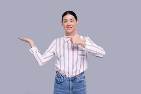 Girl Holding Hand to Side Pointing at Hand Looking into Camera Isolatedの写真素材