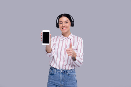 Girl Showing Phone Wearing Headphones Standing Isolated with Thumb Up. Commecial, Shopping, Advertisment Conceptの写真素材