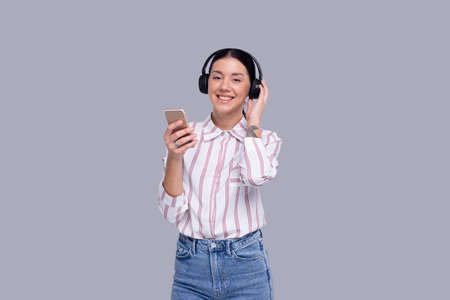 Girl Listening to Music from Phone Enjoying It Looking to Camera. Girl Listening Music with wireless headphones Isolatedの写真素材