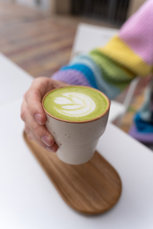 Man Hands Holding Macha Latte Cup with Wooden Plate in Caffeの写真素材