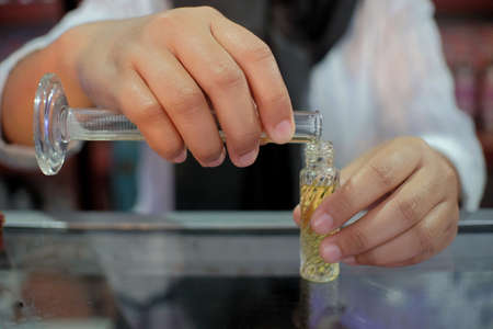 The hand of a perfume seller is pouring refillable perfume from a measuring cup into a small container.の写真素材