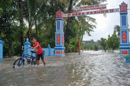 Klaten, Indonesia, Feb 5, 2021. Boy playing with his bicycle in the flood stream that overflowed from the river due to heavy rainfall.のeditorial素材