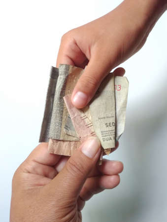 Klaten, Indonesia, Jan 25, 2021. Close up of the hands of a person giving and receiving shabby and wrinkled rupiah denominations, isolated on a white background.のeditorial素材