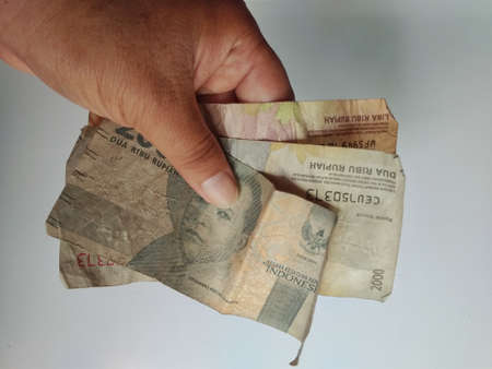 Klaten, Indonesia, Jan 25, 2021. Close up of a hand showing several banknotes of 2000 rupiah and 5000 rupiah denominations, worn and crumpled, isolated on a white background.のeditorial素材