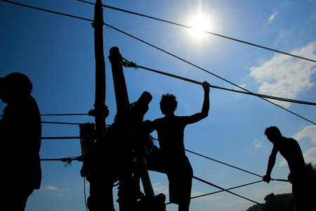 silhouette of people climbing on a rope over blue sky backgroundの写真素材