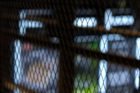 Defocused wire mesh barrier with blurred light background.の写真素材