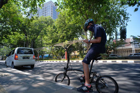 Semarang, Indonesia, Sept 19, 2020. Cyclists stop briefly on the side of a shady road due to shady trees to check their route on their smartphone.のeditorial素材