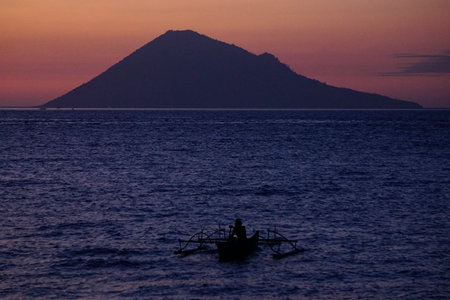 Fisherman sail alone when dusk with the background of Manado Tua Island, Indonesia