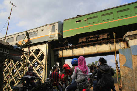 Tasikmalaya, Indonesia, June 16, 2014. The queue of vehicles that want to cross waiting for the train to pass that passes on the railroad line is above itのeditorial素材