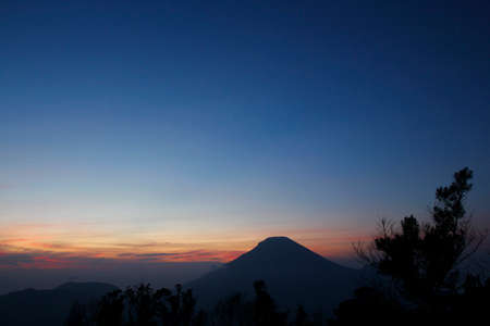 Before the sunrises Sikunir peak with a dark blue sky and a silhouette of the orange horizon line, Dieng Wonosobo, Central Java.の写真素材
