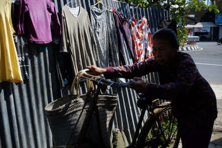 Central Java, Indonesia April 8, 2019.An old woman walked while carrying her old bicycle and carrying shopping bags on the village road, in Magelang.のeditorial素材