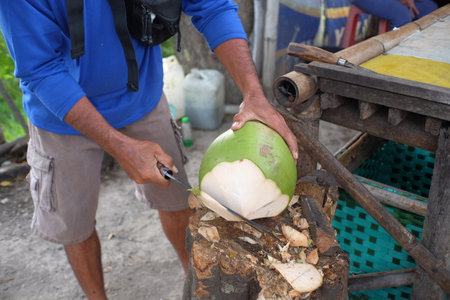 Close up of a person's hand peeling a young coconut using a machete.の写真素材