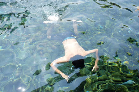 A person swimming or diving under the clear surface of the pool water.の写真素材