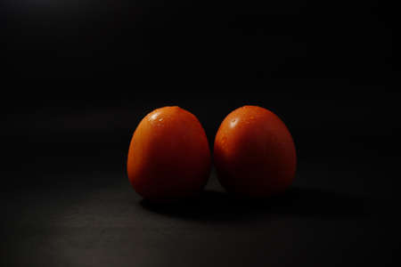Two red tomatoes with low key lighting or dominantly dark.の写真素材