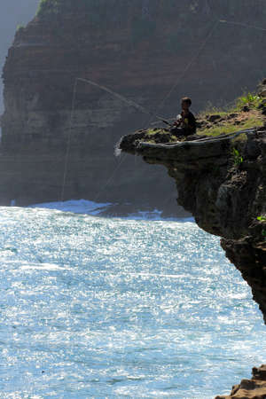 Yogyakarta, Indonesia, Jun 12, 2015. A child fills his day off by fishing on edge of the cliff of Timang Beach. The beach at Gunungkidul is famous for its cliffs and corals like the beach in Bali.のeditorial素材