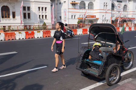 Yogyakarta, Indonesia, Aug 12, 2018. A runner girl walks past a pedicab driver who is still asleep on top of his parked vehicle.のeditorial素材