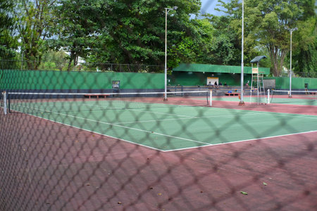 A tennis court left empty without a game behind a wire mesh guardrail.の写真素材