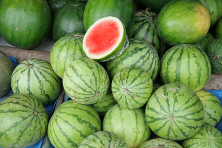 Watermelons at a stall, one of which is cut open, revealing the red inside, a sign of ripeness.の写真素材