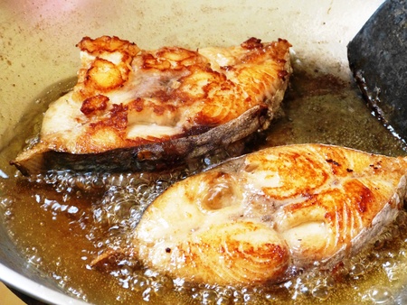 Two pieces of salmon fish cooked in a pan with oil and ingredientsの写真素材