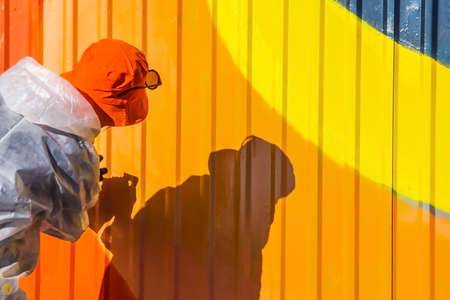 A young girl in a white coat with spots of paint paints ribbed iron fence graffitiの写真素材