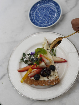 Hand holding isolated cheesecake with fresh fruits by a gold spoon in white dish on marble patternの写真素材