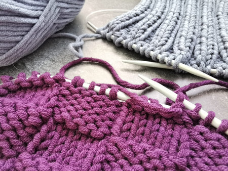 Gray and purple pieces of knitting and skeins of yarn on gray background. Knitted patterns and...